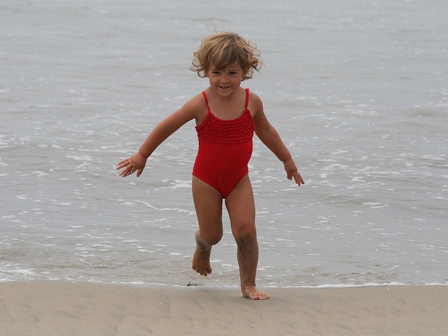 niña corriendo en la orilla bañador rojo