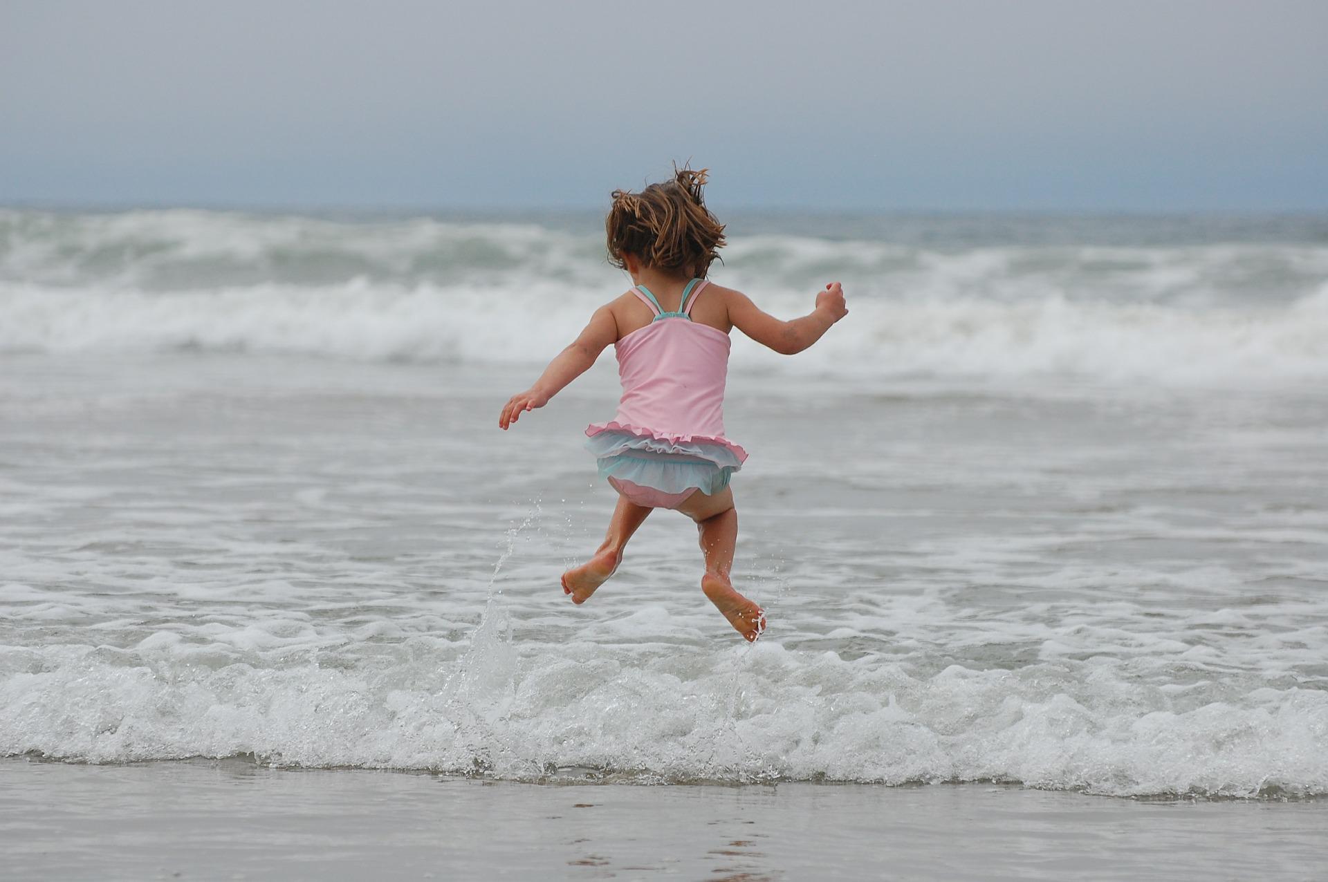 niña saltando de espaldas a cámara mirando al mar